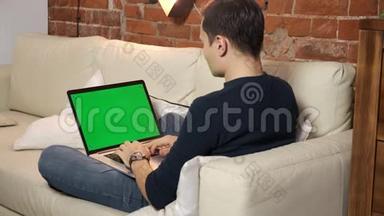 桌上的人正在绿色笔记本电脑屏幕上浏览互联网。 在一个光线充足，舒适的公寓里。 一个人在工作