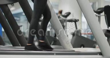 年轻女子在健身房跑步机上行走。 热身或<strong>降温</strong>.. 腿侧视近景拍摄，下身细节.. 妇女