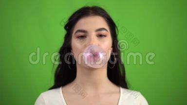 微笑的女孩在绿色的屏幕上吹泡泡糖，嚼着粉红色的泡泡糖