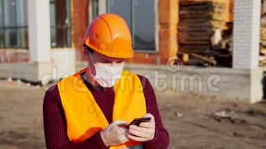穿着工作服、戴着医用口罩的男建筑工人在手机上翻翻有关冠状病毒的新闻