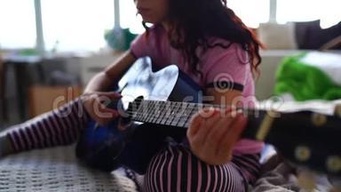 年轻女子在卧室弹吉他。 年轻女子在床上弹吉他。 她喜欢业余时间。 美丽美丽
