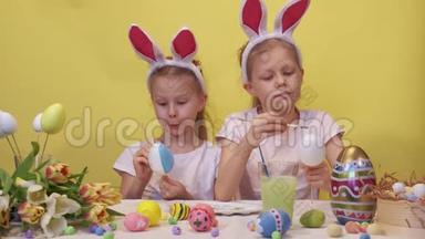 专注的姐妹，兔子耳朵站在桌子附近，调色板和郁金香花束仔细着色鸡蛋，而