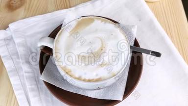卡布奇诺或拿铁。 咖啡与泡沫牛奶在<strong>圆形</strong>杯与棕色茶托和勺子是在<strong>桌子</strong>上。 用奶油泡沫喝。 特写