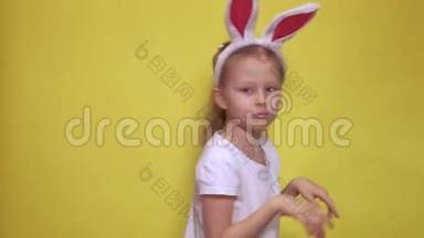 可爱的小女孩，长着小兔子的耳朵，看着摄像机，一边跳着，一边假装在复活节庆祝活动中是兔子