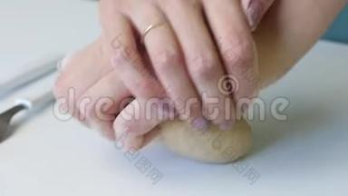 一个女人用手捏一块面团做新鲜蛋糕。 桌子表面附近有擀面杖和面粉..