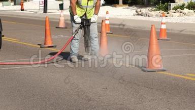 作为公用事业的一部分，工作人员在橙色安全警示锥旁边的一条城市街道的沥青上使用了一把手提锤