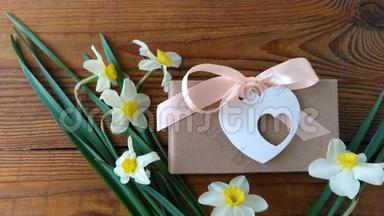 白色水仙花和棕色礼盒，贺卡用粉色丝带<strong>放在木质</strong>背景4K视频上.. 女人的手放花