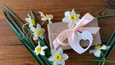 白色水仙花和棕色礼盒，贺卡用粉色丝带放在木质背景4K视频上.. 女人的手放花