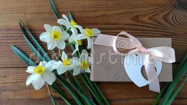 白色水仙花和棕色礼盒，贺卡用粉色丝带放在木质背景4K视频上.. 女人的手放花