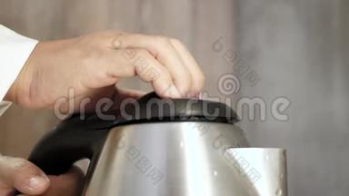 女人的手拿着厨房里的<strong>电水壶</strong>，准备热饮料，点击按钮。