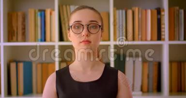 年轻成功的红头发女学生戴着眼镜，在室内看着图书馆里的摄像机