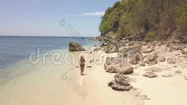 阳光明媚的一天，快乐的年轻女子在热带岛屿的沙滩上奔跑。 鸟瞰欢快的女人在奔跑