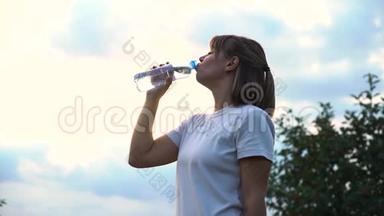 年轻漂亮的运动女孩穿着一件白色T恤，<strong>很累</strong>，喝着透明瓶子里的水，慢动作