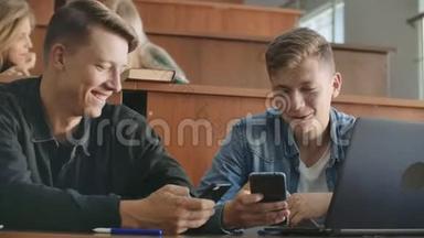 在大学演讲的休息时间，手持智能手机的男生在观众中大笑