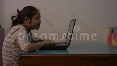 亚洲可爱的女孩学生戴着耳机，在网上学习课程时与笔记本电脑老师交谈。