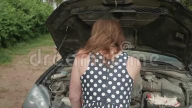 后面的女孩穿着有斑点的衣服，靠近汽车，带着打开的引擎盖。 女孩笑着转过身来，擦了擦额头