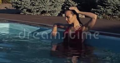 穿红色衣服的女人正在抚摸她湿漉漉的头发，在游泳池里摆姿势，4K