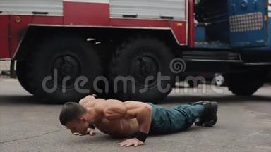 慢动作。 漂亮的赤膊青年运动员，用跳跃练习俯卧撑。 背景中的大型消防车