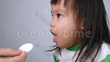 <strong>生病</strong>的<strong>小女孩</strong>吃药，在卧室里用勺子止咳糖浆。 儿童保健和医疗的概念。