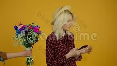 戴<strong>帽子</strong>的金发女孩使用智能手机，拒绝<strong>黄色</strong>背景的花束