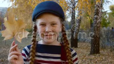 肖像少年女孩，手里拿着黄色枫叶，近脸。 微笑着面对秋天公园里快乐的女孩。 红色