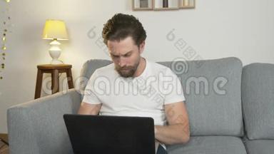 一个年轻人独自坐在家里的沙发上，坐在笔记本电脑上，上网冲浪，因为
