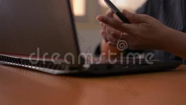 女人的手在电脑键盘上打字，用手机，女商人在办公室里用笔记本电脑工作。
