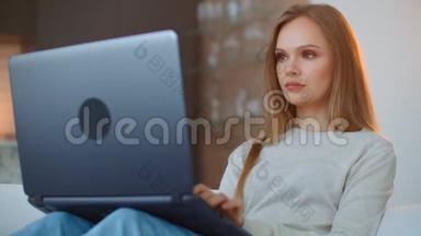 年轻女孩带着<strong>笔记本电脑</strong>坐在家里的沙发上。 在沙发上躺着的<strong>笔记本电脑</strong>键盘上打字，沙发在