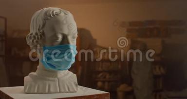 戴着医疗面具的名人的白色石膏雕塑头站在雕塑家工作室的小桌子上。 被征服