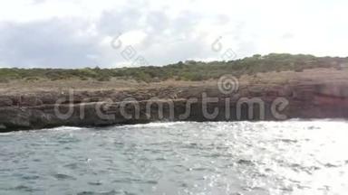 天晴：看海浪冲击岩石，悬崖海岸在阳光明媚的一天，男人坐在岩石上马洛卡岛阳光明媚