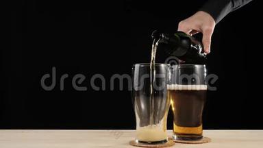新鲜啤酒。 手把美味的手工啤酒倒在第二杯啤酒杯上，从棕色的瓶子里倒入木桌上，放在黑色的桌子上