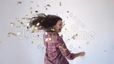 美丽的快乐女孩跳舞和投掷金色纸屑。 慢动作