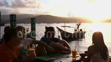 朋友们坐在山上的咖啡馆里俯瞰大海，令人惊叹的日落喝鸡尾酒。 慢动作