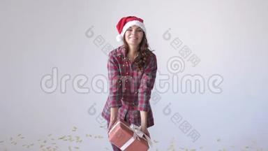 穿着圣诞帽和睡衣的快乐女孩在白色背景下扔礼物盒等待假期。 慢动作