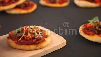 女人的手把自制的迷你披萨放在黑板上。 迷你比萨饼，上面有火腿、绿色橄榄、樱桃番茄和新鲜罗勒