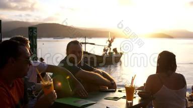 朋友们坐在山上的咖啡馆里俯瞰大海，令人惊叹的日落喝鸡尾酒。 慢动作