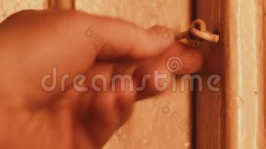 晚上，一个男人`手打开一扇锁在钩子上的房子里的木门。 白炽灯光。 木门被粉刷了