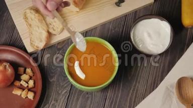 奶油南瓜汤烹饪。 Ð把酸奶油放在奶油南瓜汤里，放在绿色的碗里，放在装饰好的木桌上。 上景。 4K.