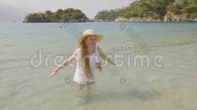 无忧无虑的女孩在天堂海滩泼海水。 戴着草帽的快乐女孩站在清澈的海水中