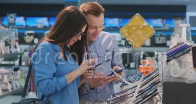 一个年轻的男人和女人手里拿着两部智能手机，站在一个电子产品智能手机陈列柜旁