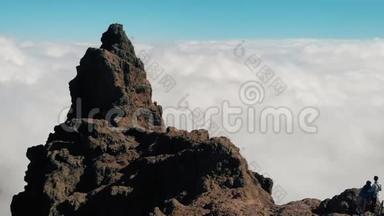 空中观景。 一对年轻夫妇站在云层上方的悬崖边上。 镜头移向上方的一个大悬崖