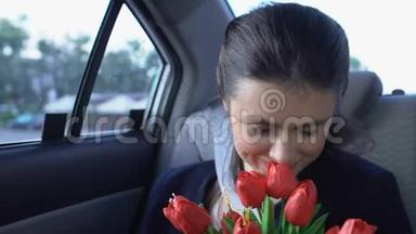快乐的女孩坐在车里闻花，满意的出租车客户享受乘车