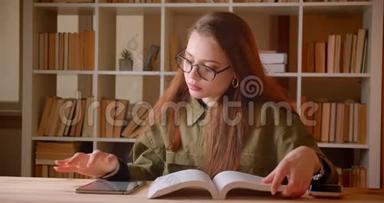 年轻女学生阅<strong>读书籍</strong>和在平板电脑上搜索信息的肖像，在图书馆做作业。