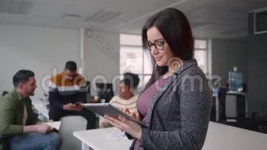 在背景中看到了快乐年轻、有魅力的女商人与同事一起使用数码平板电脑的画像
