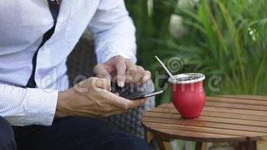 男人用智能手机和喝耶尔巴伴侣茶。 动作缓慢。