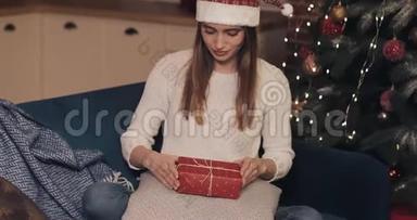 靠近迷人的女孩，穿着毛衣和圣诞帽，坐在圣诞树附近的沙发上，最后<strong>敲定</strong>了一个大的。