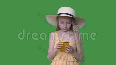 戴帽子和穿黄色衣服的年轻女孩在透明的绿色背景上使用手机。 有头发的夏天女孩