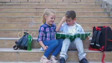 学校里的小学生背着背包坐在台阶上，在露天休息时<strong>翻阅</strong>一本书