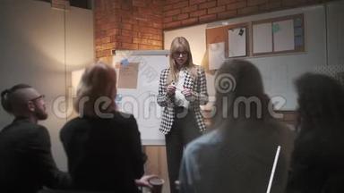 女经理在会议上向同事介绍新的项目计划，并向办公室同事解释有关挂图的想法