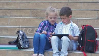 在户外课间休息时，现代学龄儿童、小女孩和小男孩在背包附近的台阶上使用数字平板电脑